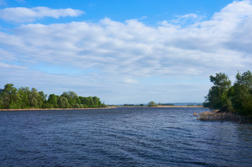 Obraz premium A river on a sunny summer day with trees on the shore and a beautiful sky in the clouds.