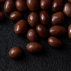 Chocolate candy background. Dark brown chocolate round candies on black concrete background  top view, close up.