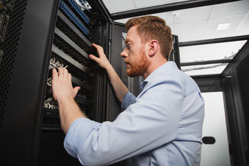 Computer equipment. Low angle of determined IT technician studying server closet while standing