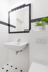 Mirror above washbasin in white and black bathroom interior with plant. Real photo