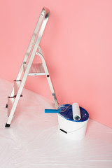 close up view of paint roller on paint tin and ladder in front of painted wall