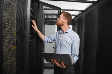 Computer programming. Confident IT technician examining server closet while carrying laptop