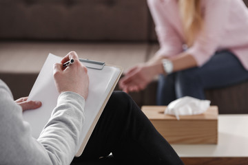 Close-up of therapist hand writing notes during a counseling session with a single woman sitting on...