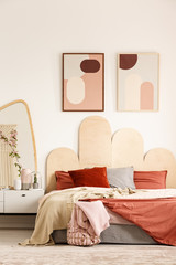 Posters above orange bed next to white cabinet with mirror in modern bedroom interior. Real photo