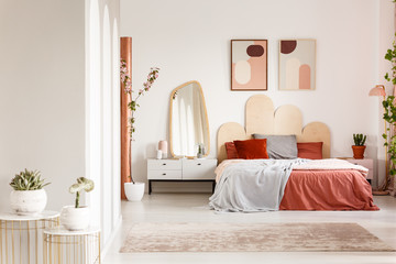 Mirror on white cabinet next to orange bed under posters in modern bedroom interior. Real photo