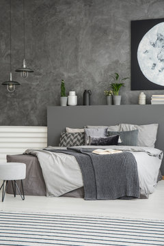 Grey sheets on bed in monochromatic dark bedroom interior with poster on the wall. Real photo