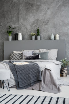 Dark blanket on bed with headboard in grey bedroom interior with concrete wall. Real photo
