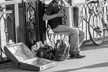 Fototapeta na wymiar Old man playing accordion on the bridge and trying to earn money. A man asks for money for playing the accordion. Black and white photo