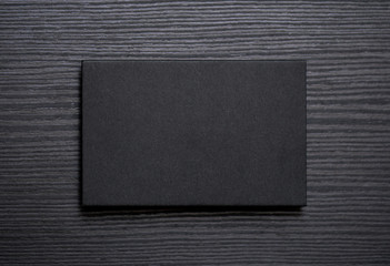 Mockup of blank textured black business card on dark wood background