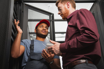 No problem. Low angle of professional two colleagues standing near server closet and communicating
