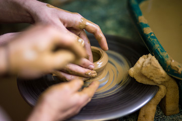 Close-up hands of potter in apron making vase from clay, selective focus. Making it together. Top view of potter teaching to make ceramic pot on pottery wheel