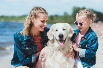 attractive mother and smiling daughter with golden retriever dog on sea shore