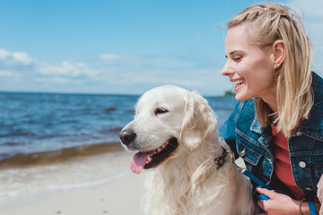 beautiful smiling woman sitting with golden retriever dog on sea shore