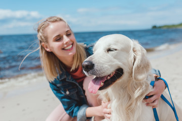 happy attractive woman sitting with golden retriever dog on sea shore