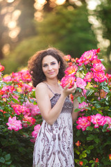 Portrait of a young Caucasian woman near red and pink roses bush in a rose garden, looking to the camera