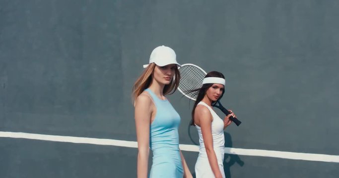 Portrait of two young Caucasian teen models wearing fashionable tennis dresses, passing by and looking into camera, summer sunny day outdoors. Fashion portrait shoot
