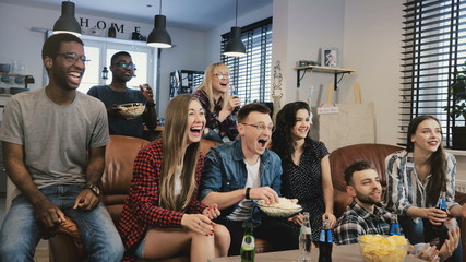 Multi-ethnic friends watching TV show. Medium shot. Diverse team supporters passionate and...