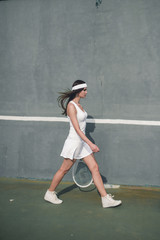 Fototapeta na wymiar Portrait of young Caucasian teen model wearing fashionable tennis dress, walking on tennis hardcourt, summer sunny day outdoors. Fashion portrait shoot