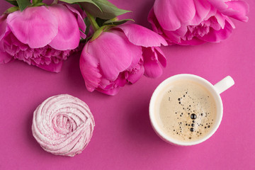 white beautiful cup with a drink of coffee with foam on a pink background, pink blueberry marshmallow and pink peony flowers, concept of morning, lifestyle and breakfast