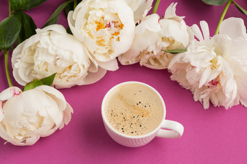 white beautiful cup with a drink of coffee with foam on a pink background and white peony flowers, concept of morning, coffee and breakfast, macro photography