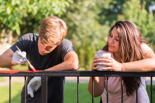 Young Man And Girl Are Painting Metal Fence With A Brush