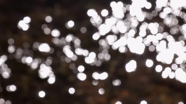 Slow Motion Of Defocused Rapid Water, Flowing Over Brown Boulders And Pebbles With Play Of Sun Reflection. High Speed Camera Shooting Of Blinking Bright Specks. Relax View For Meditative Intro.