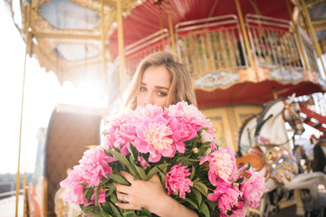 Beautiful girl in a dress with a bouquet of pink peonies in the hands near a vintage carousel	