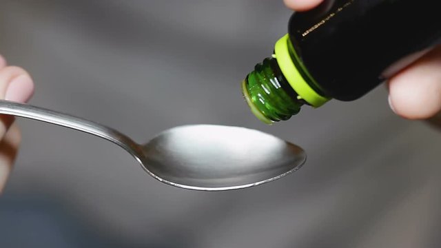 Lady pours six drops of laxative out of jar on metal tablespoon and swallows it