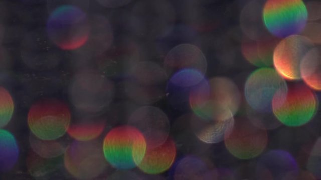 Abstract bokeh holiday background. Decoration of playing colored light in slow motion. Christmas and new year iridescent lights on dark background. Rainbow of defocused crystal bead hangings in HD.