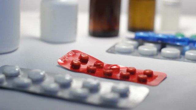 Patient takes pills one by one. Hand takes next package of tablets off table