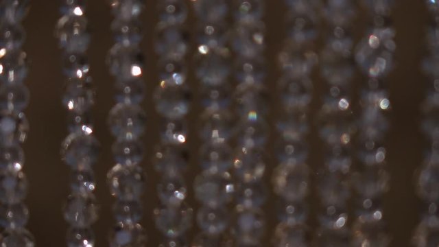 distance panorama with shallow focus of crystal bead hangings, sparkling on brown background. Play of sharpness in slow motion. Abstract backdrop with changing bokeh and multicolor light.