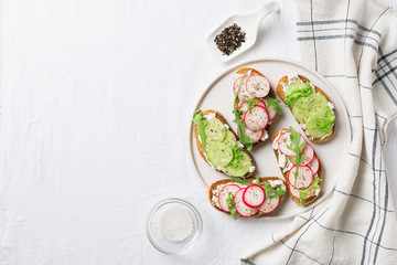 Some radish and cucumber toasts with ricotta and salad on plate with salt and paper