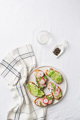 Some radish and cucumber toasts with ricotta and salad on plate with salt and paper