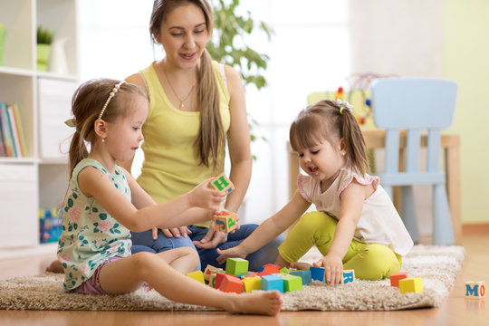 Family mom and children daughters playing with block toys in living room