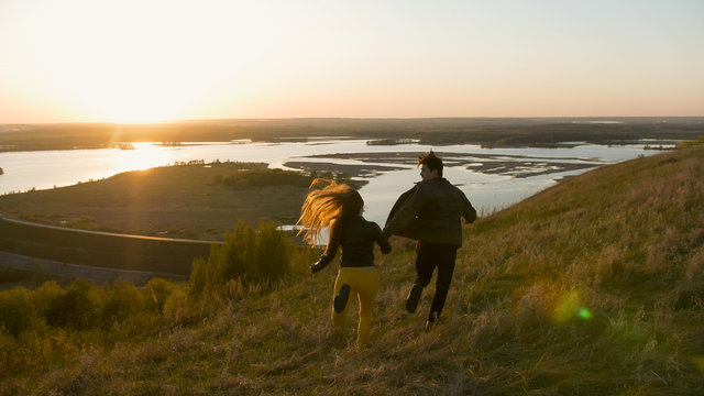 Happy young couple running on the hill holding hands at sunset