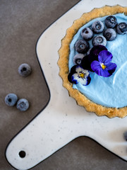 homemade pie with blueberries and almonds crust, decorated with Pansy flowers. places in a white ceramic plate on grey background.