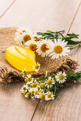 Yellow soap on sackcloth with bouquet of fresh chamomiles on wooden boards