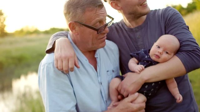 Three generations of one family embrace. Men rest on the river bank. Grandpa, son and grandson spend time together. Happy family vacation