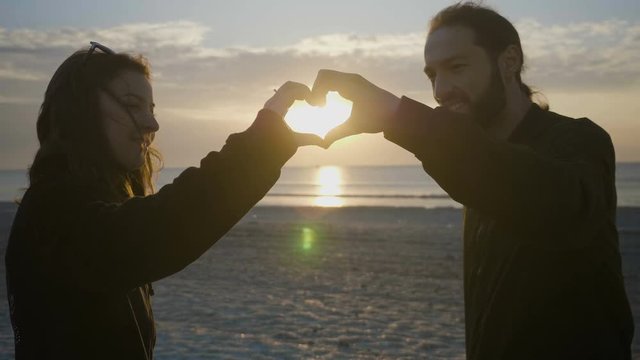 Teenage couple making a heart shape with their heads on the beach before sunset