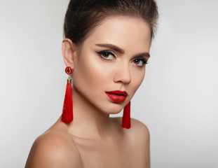 Beautiful girl with earrings jewelry. Beauty face of young brunette woman with a bright make-up and red lips isolated on studio background. Fashion, make-up, cosmetics, hairstyle.