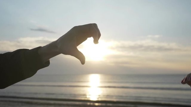 Close up of two lovers hand making a heart shape on a sunrise beach in slow motion