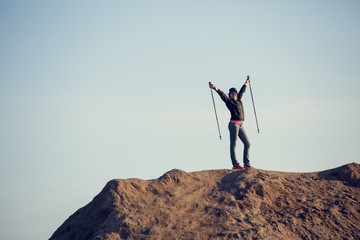 Full-length picture of woman growing tourist with backpack and walking sticks with hands up on mountain