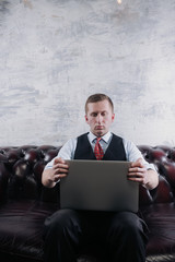 Serious self employed man working on the laptop. Businessman sitting on couch and using laptop