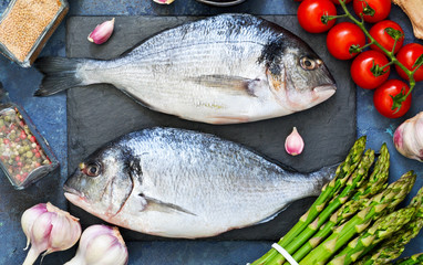 Fresh, raw Dorado fish with asparagus, tomatoes and spices on a concrete background. Ingredients for cooking.