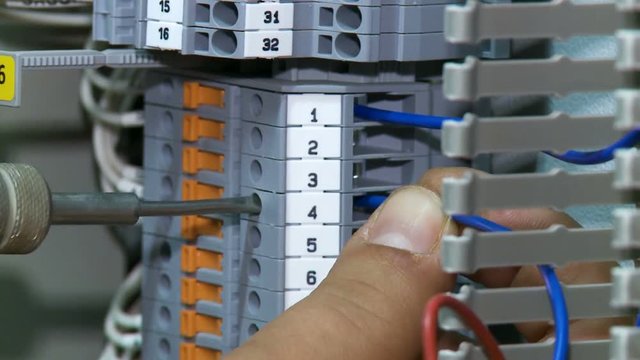 man twists screw on switch board with blue wires