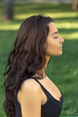 Close-up profile portrait of fitness girl. Young girl doing yoga in the park. Woman practicing yoga performing lotus position outdoors with closed eyes. Young attractive slim girl in bodysuit relaxing