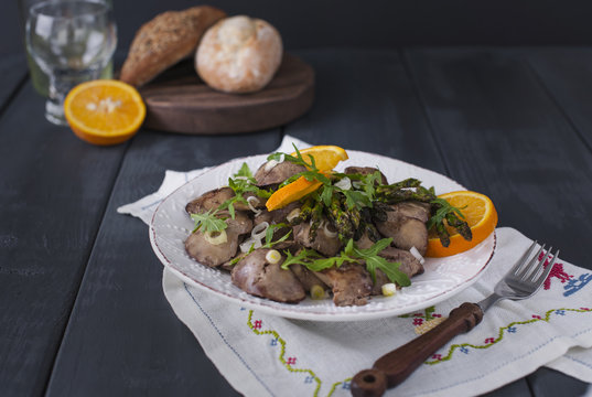 A delicious healthy dinner, a warm chicken liver salad with oranges and rucola, on a black wooden background. Free space for text. Copy space.