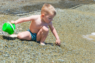 A little boy in swimming trunks is playing on the beach.