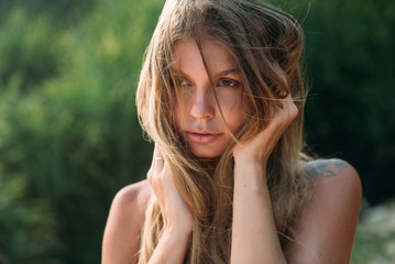 A close view of a beautiful tender sweet girl starts her hands in her hair, looks into the distance and dreams. A model with bare shoulders and brown eyes, the wind blows her hair.