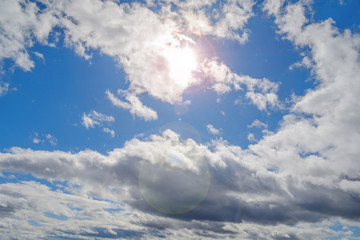 Abstract blue cloudy sky on bright day with sun flare